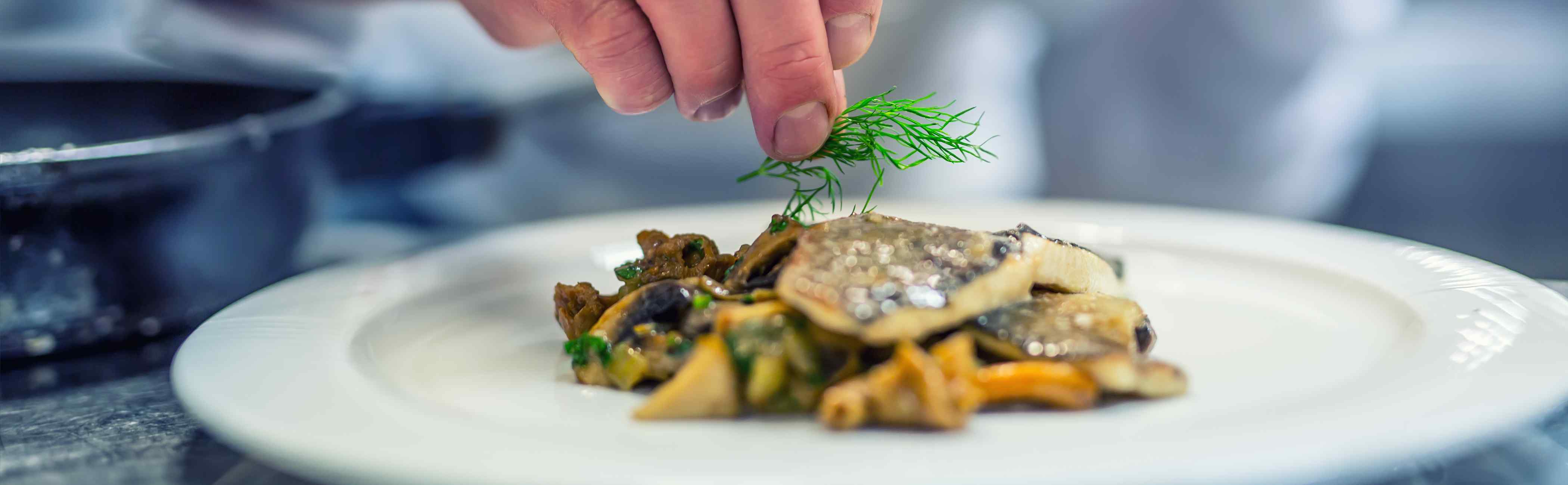 A hand sprinkling garnish onto a plated fish dinner.